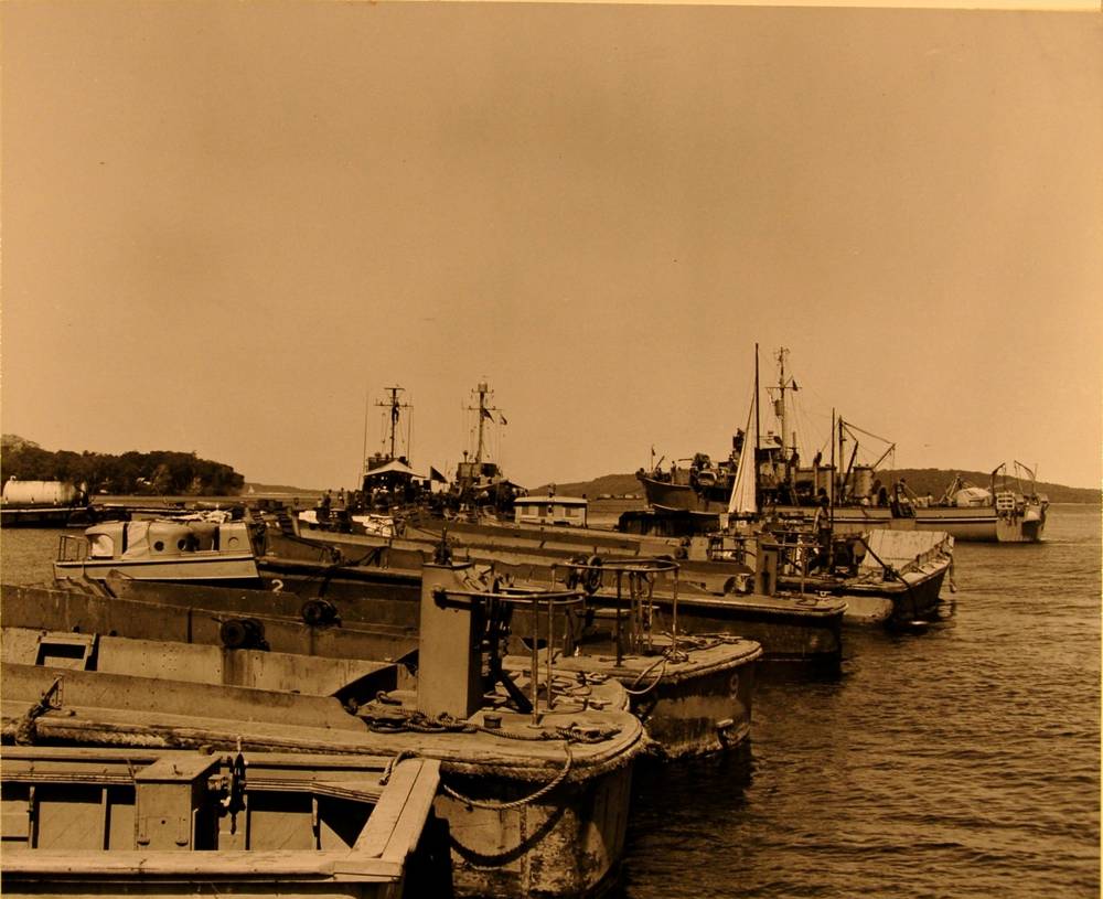 Landing craft moored together in the harbour, ships behind
