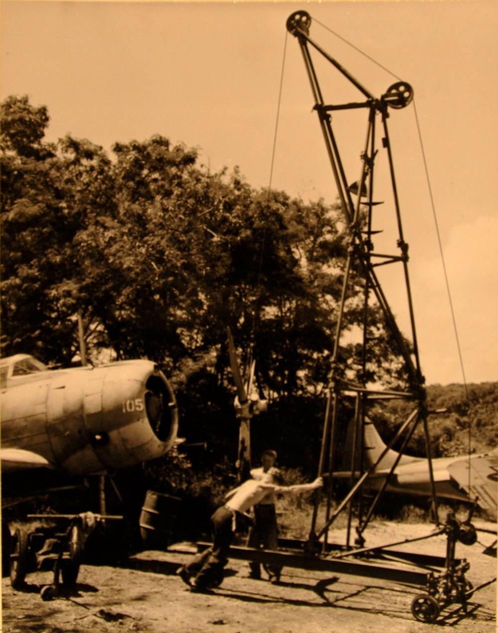 Two Navy mechanics using a wheeled gantry to lift the propeller off a Dauntless dive bomber numbered 105