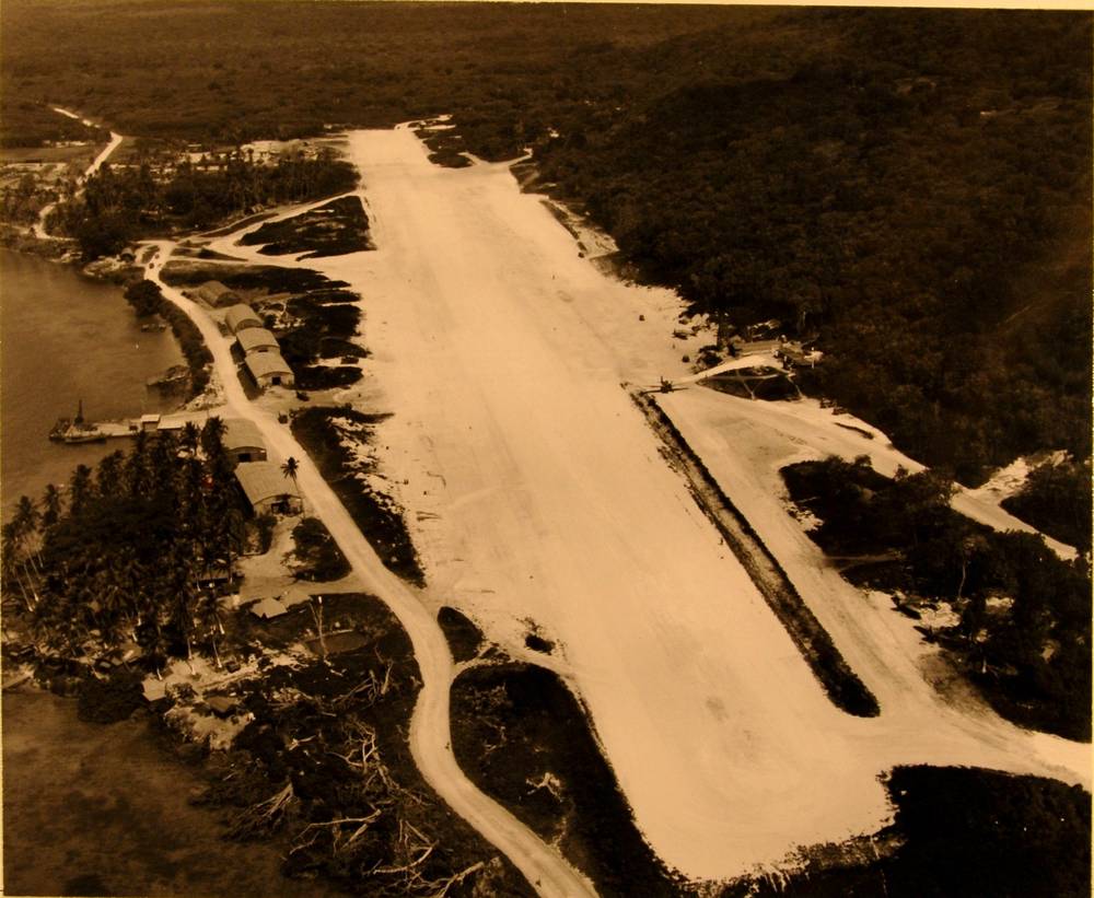 Aerial view along the white coral runway, hangars beside the harbour road